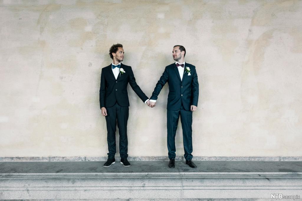 Eit homofilt par kledd til vigsel held hender. Foto. 