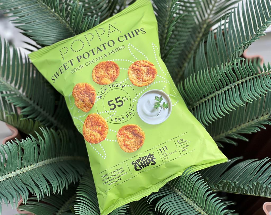 En lysegrønn pose med Poppa Sweet Potato Chips fra Sørlandschips ligger på palmeblader. Foto.