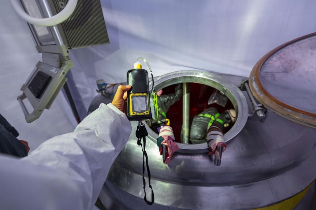 To arbeidere er inne i en tank og en står på utsiden og gjennomfører gassmåling av arbeidsmiljøet i tanken. Foto.