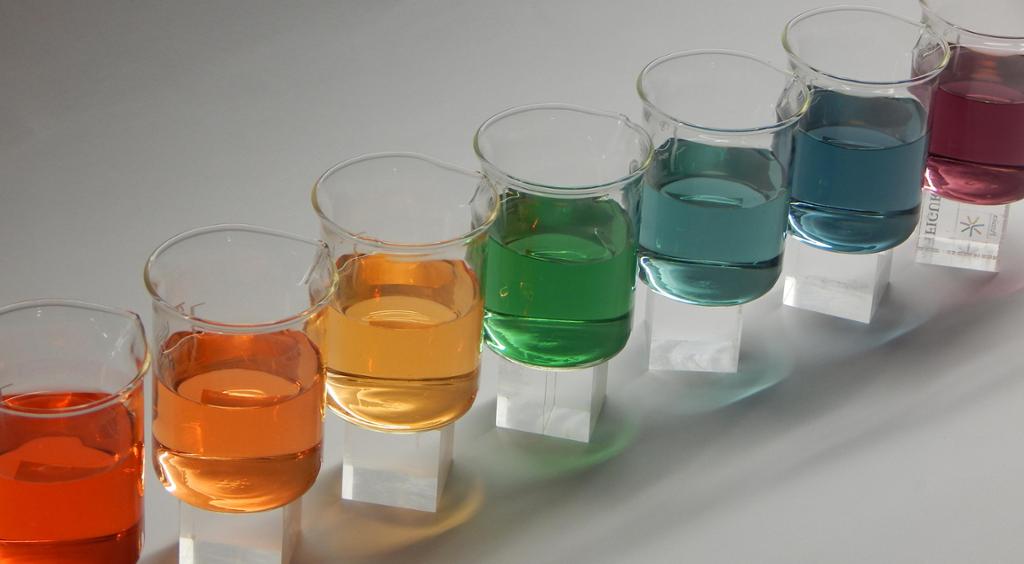 Begerglas med væske i ulike fargar står på rekke. Foto.
