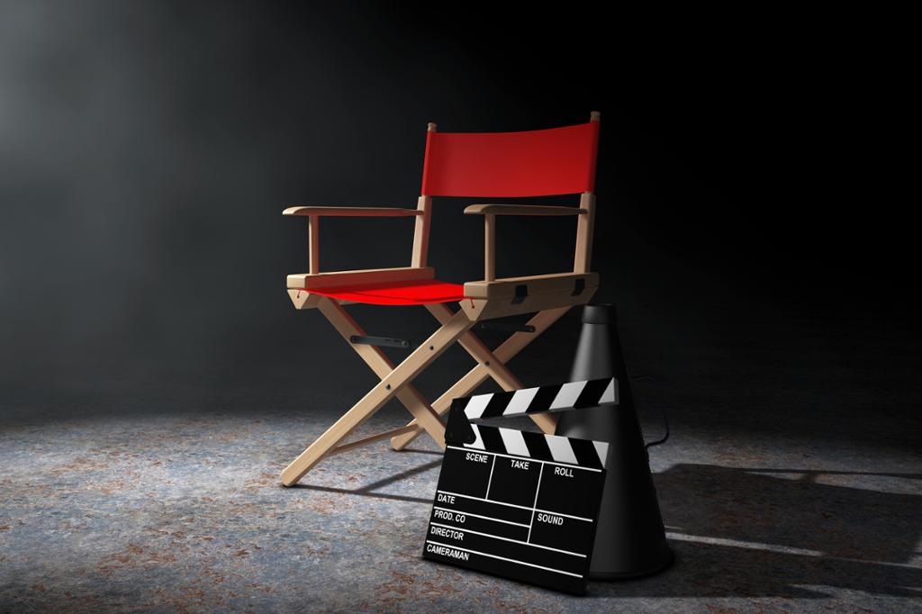 Filmproduksjonsutsyr står oppstilt i lyset fra en lyskaster. En regissørstol, en megafon og en "klapper". Digital illustrasjon.