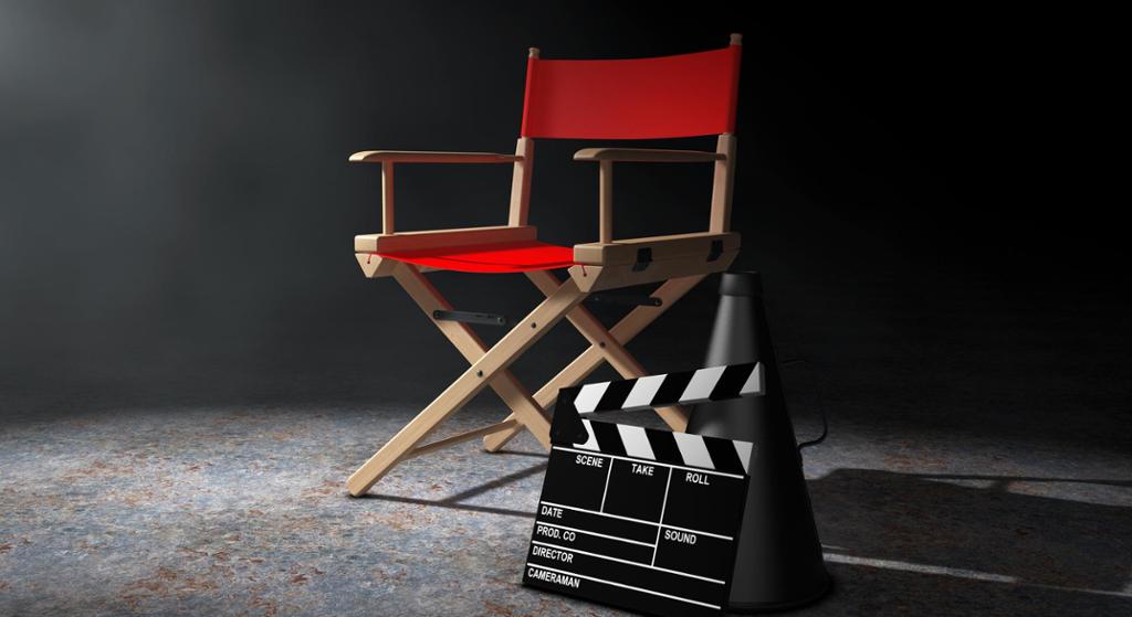 Filmproduksjonsutsyr står oppstilt i lyset fra en lyskaster. En regissørstol, en megafon og en "klapper". Digital illustrasjon.
