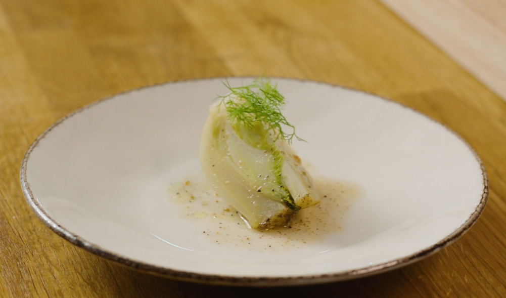 Ein bit bakt fennikel pent lagt opp på tallerken med fennikelgras på toppen. Foto.