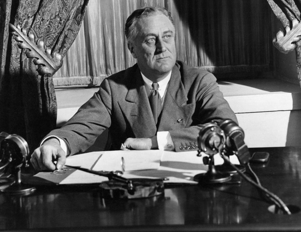 President Franklin D. Roosevelt sitter ved pulten sin i Det hvite hus i Washington D.C. Han kringkaster sin første radiotale om bankkrisen. Foto.