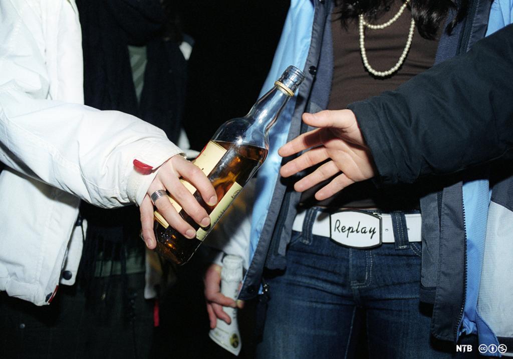 Tre ungdommar deler ei flaske sprit. Foto.
