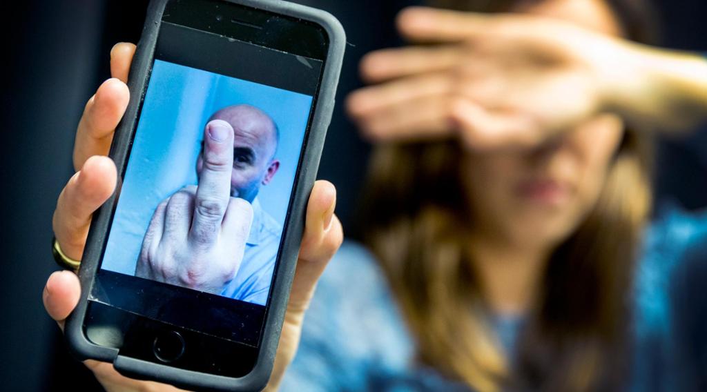 Foto av en kvinne som viser fram mobilskjermen sin. Skjermen har et bilde av en mann som viser fingeren. 