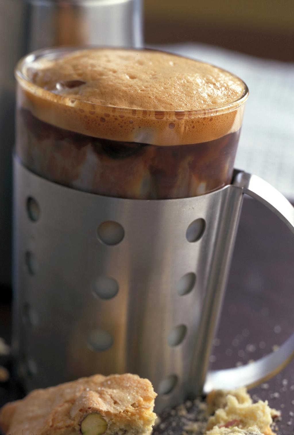 Svart kaffe med skum. Foran kaffekoppen ligger det kjeks. Foto.
