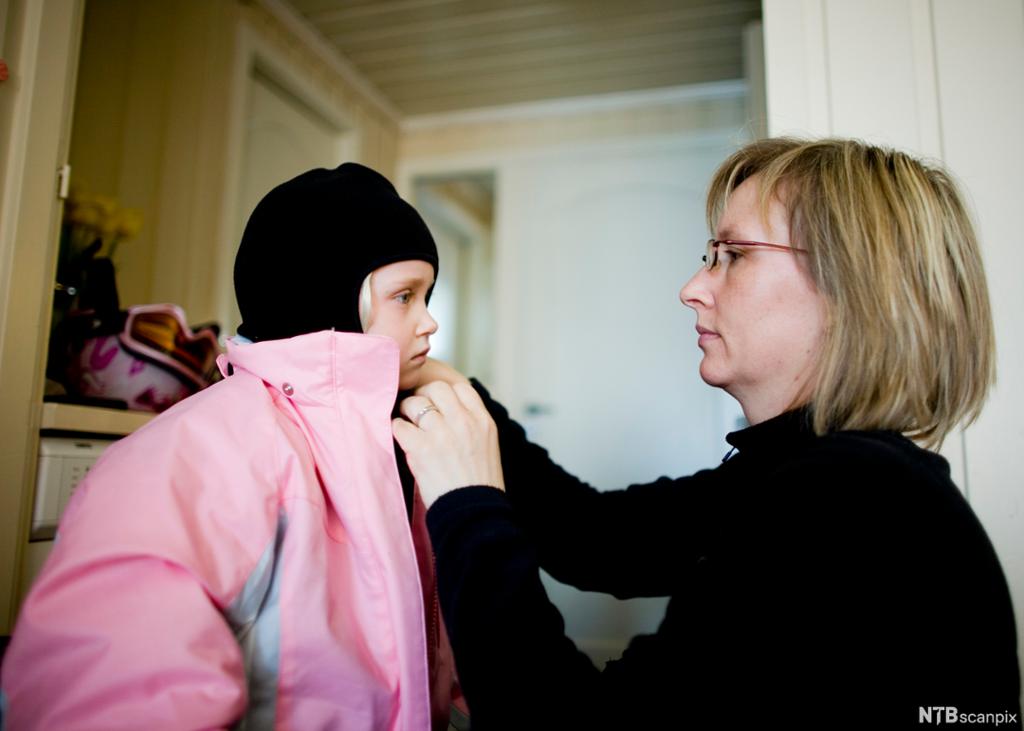 En voksen kvinne som hjelper ei jente med påkledning av yttertøy. Foto. 