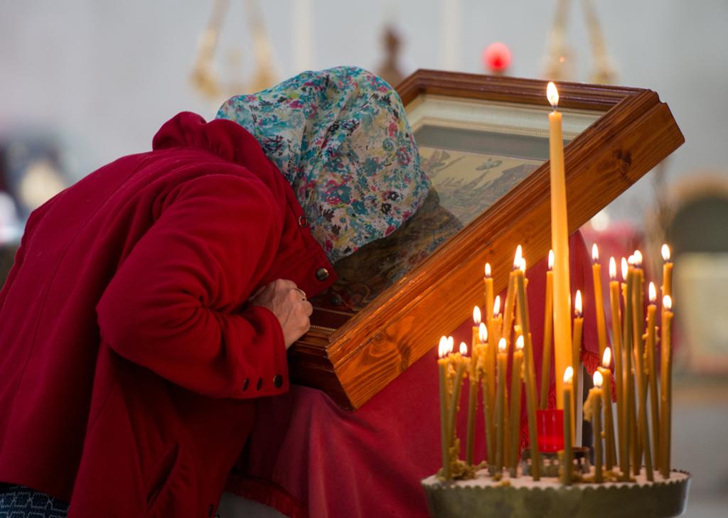 Kvinne kysser helgenbilete i ei russisk-ortodoks kyrkje. Foto.