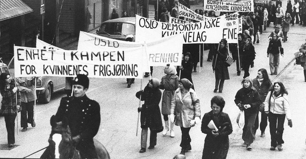Kvinner med paroler under 8. marstoget i Kvinneåret 1975. Politi til hest først i toget. Foto.