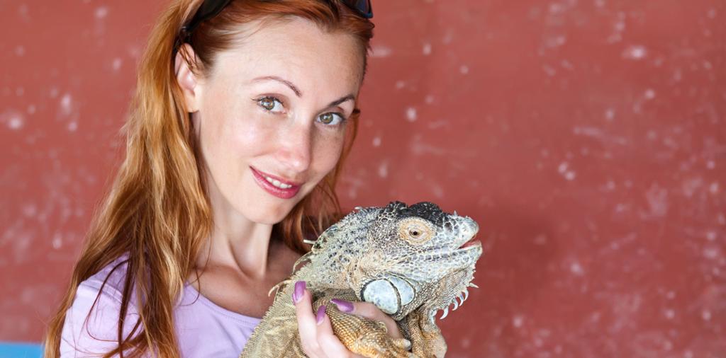 Ung kvinne med rødt hår holder en iguana. Foto.