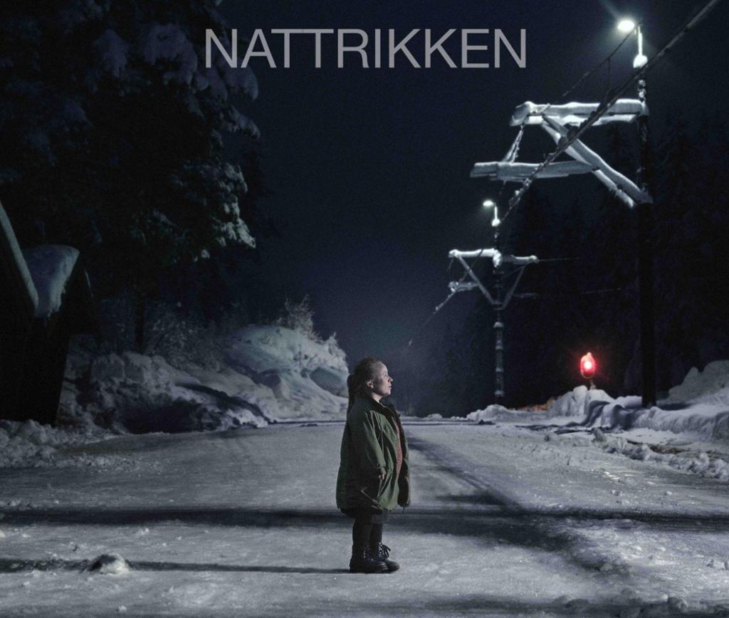 Filmplakat for kortfilmen Nattrikken. Biletet viser ei kortvaksen kvinne som ein sein kveld står ved eit trikkespor i eit snødekt landskap. Filmplakat.
