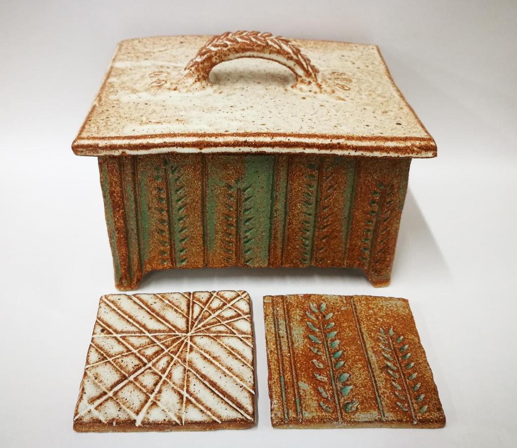 Keramikkskrin med lok og to fliser med utprøving av tekstur. Foto.