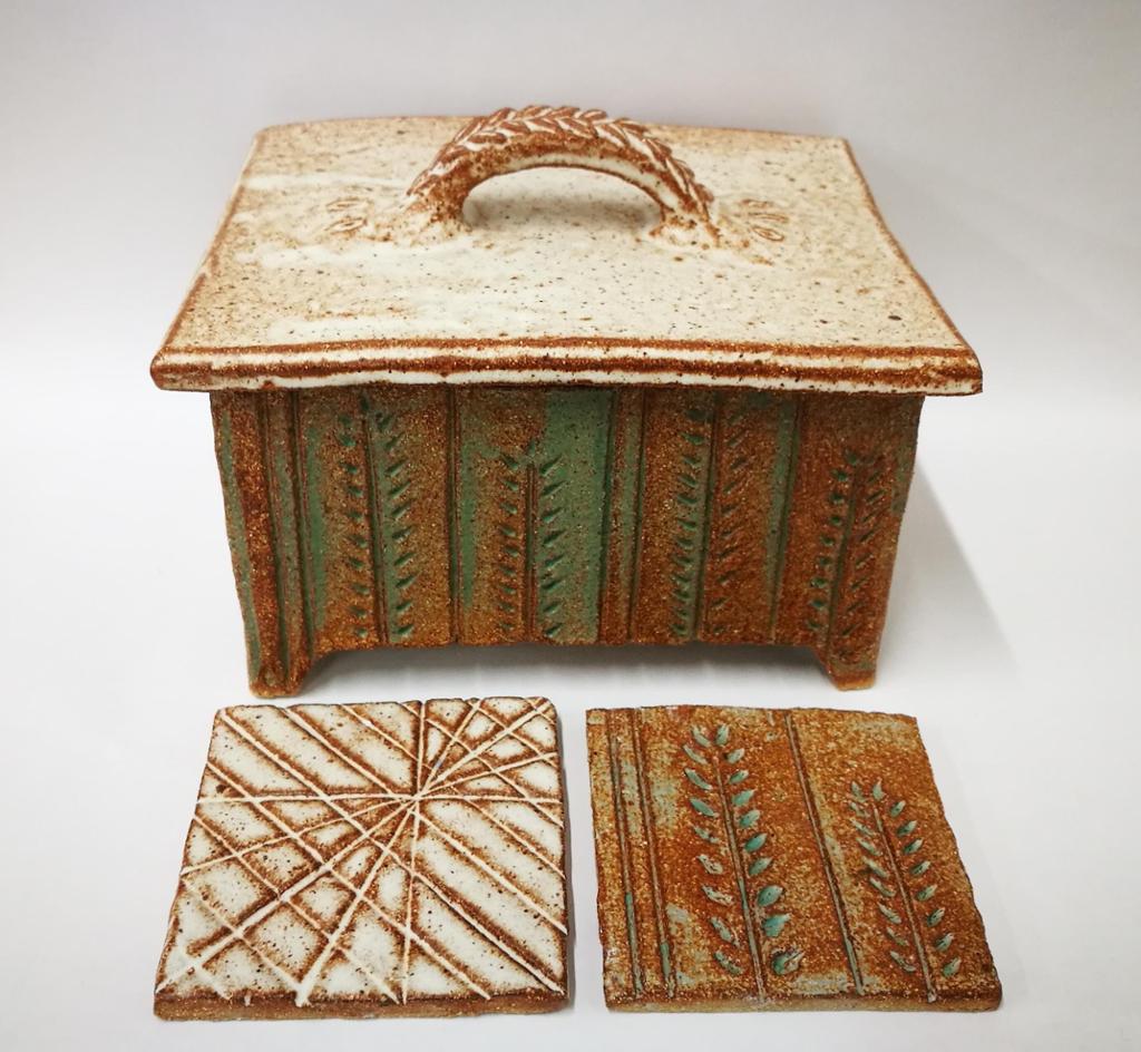 Keramikkskrin med lokk og to fliser med utprøving av tekstur. Foto.