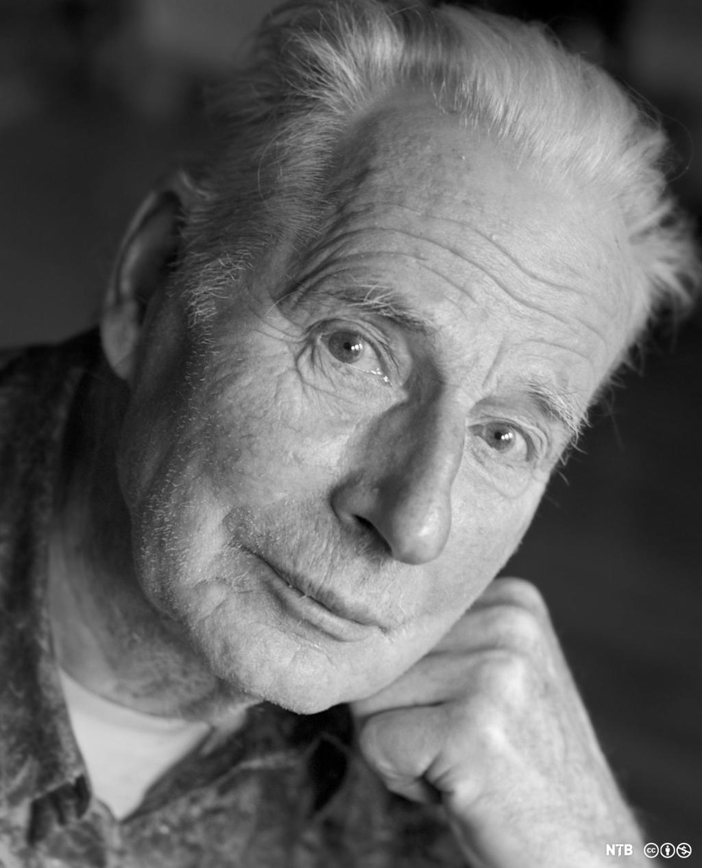 Portrett av Arne Næss, en gammel mann med kort hvitt hår, som støtter ansiktet mot knyttneven. Svart-hvitt-foto.