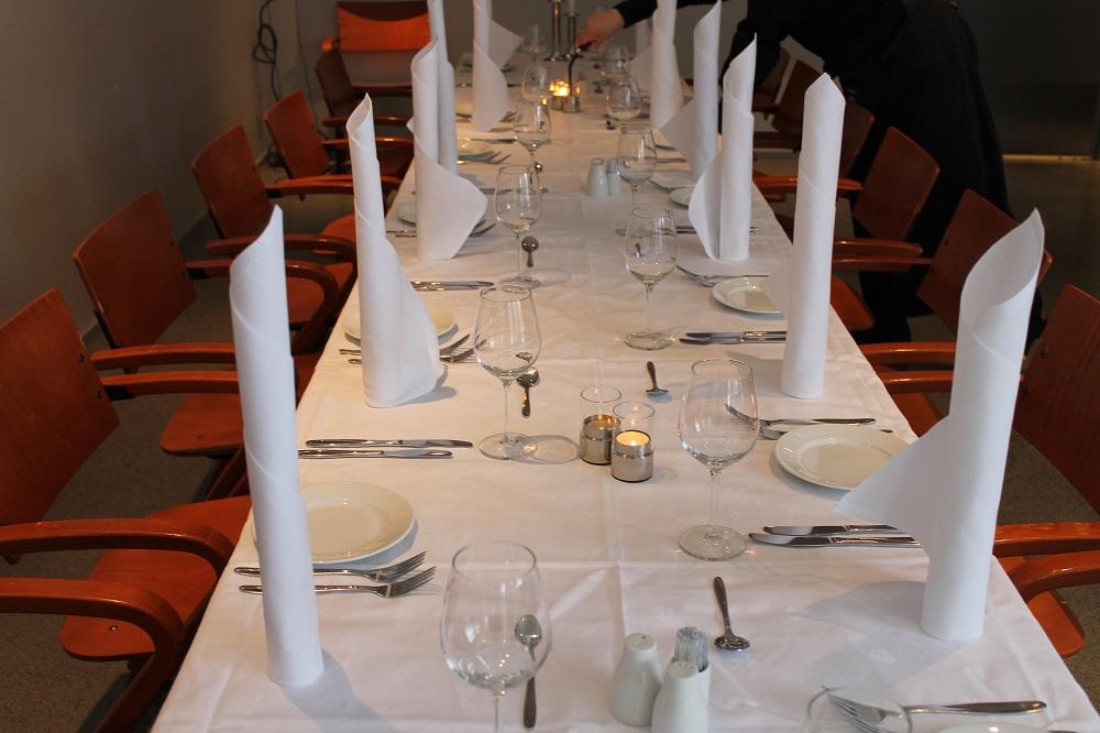 Et langbord er dekket opp til fest med vinglass og stilig brettede servietter. Foto. 