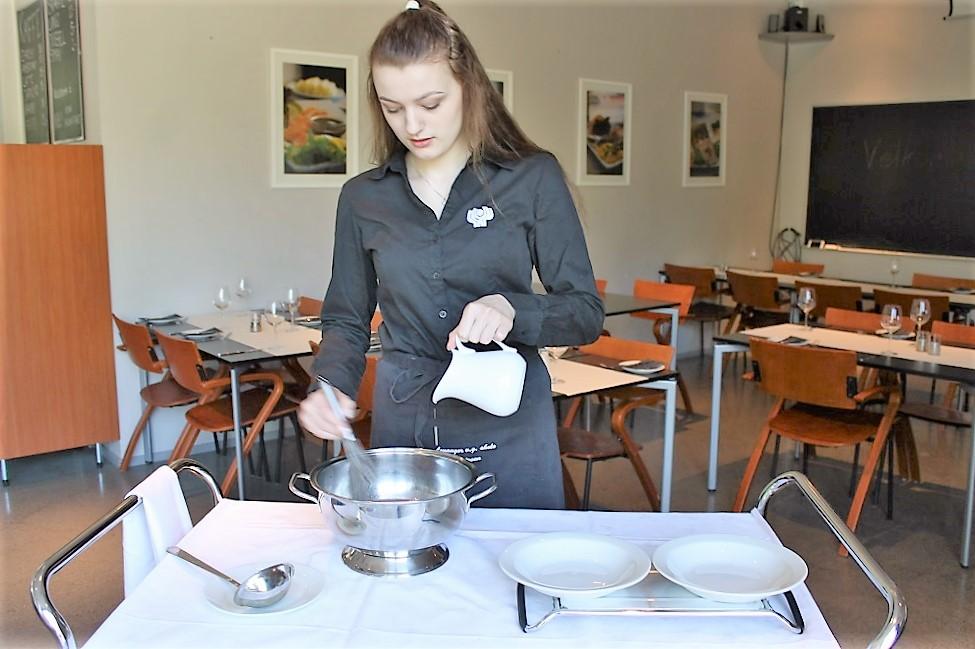 Servitør legerer suppe ved bordet til gjesten.