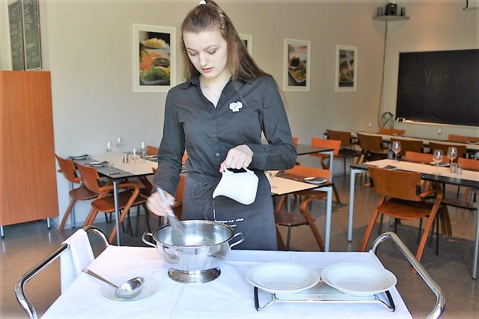 Servitør legerer suppe ved gjestens bord. Foto.