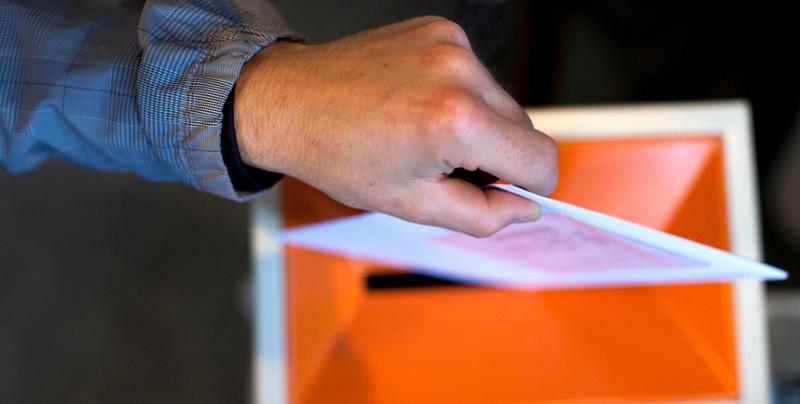 Hånd legger stemmeseddel i valgurne. Foto.