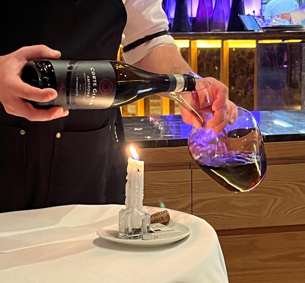 Ein servitør dekanterer ei flaske vin. Foto.