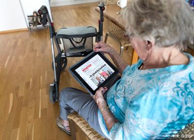 Eldre dame med rullator leser avis på iPad