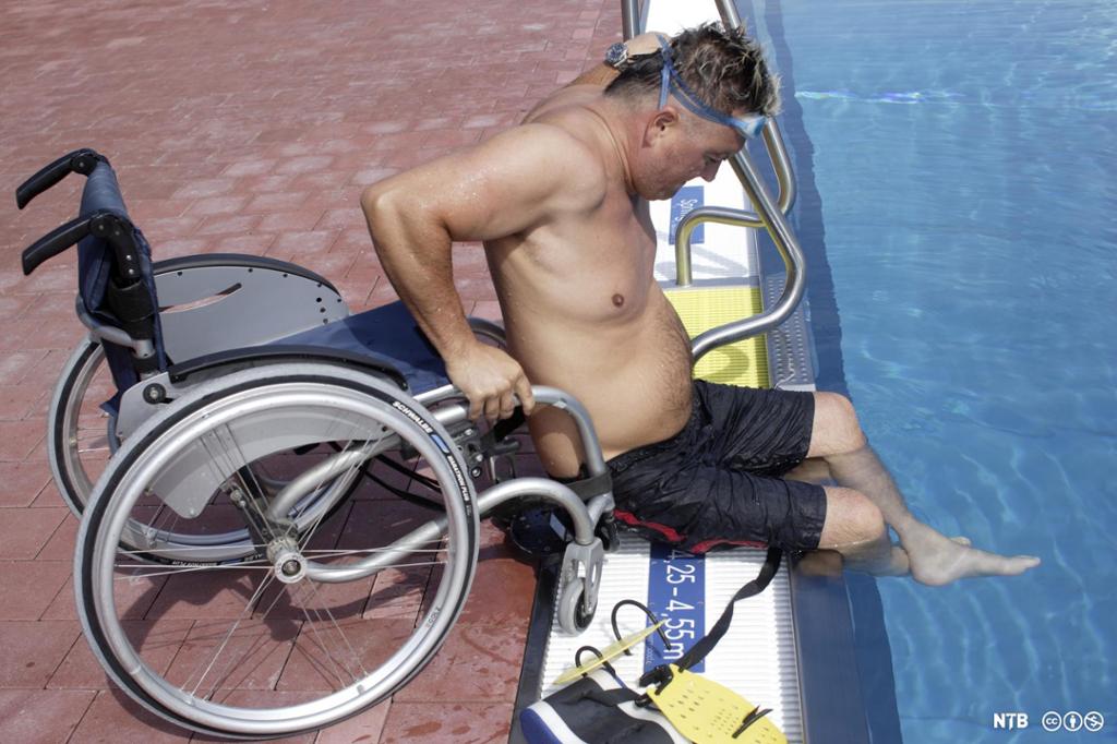 Mann beveger seg ved eiga hjelp frå rullestol til basseng. Foto.