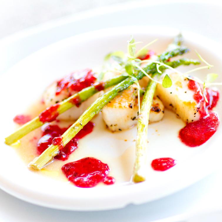 En tallerken med hvit fisk, asparges og rød saus. Foto.