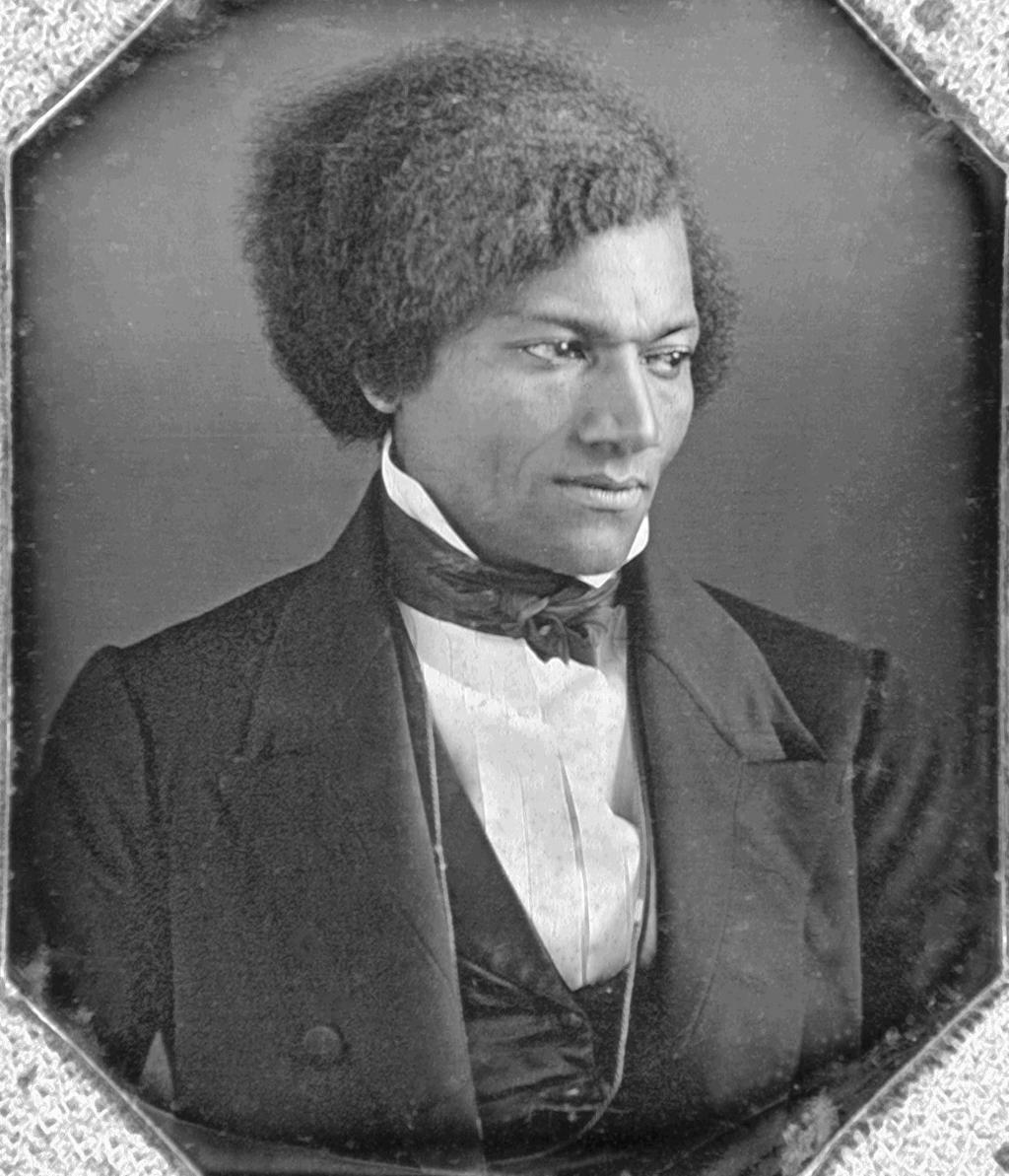 Photo: Black and white portrait of Frederick Douglass. He is wearing a stylish black suit, vest, and tie, a white shirt. He has wavy. black hair. He looks to the right. 