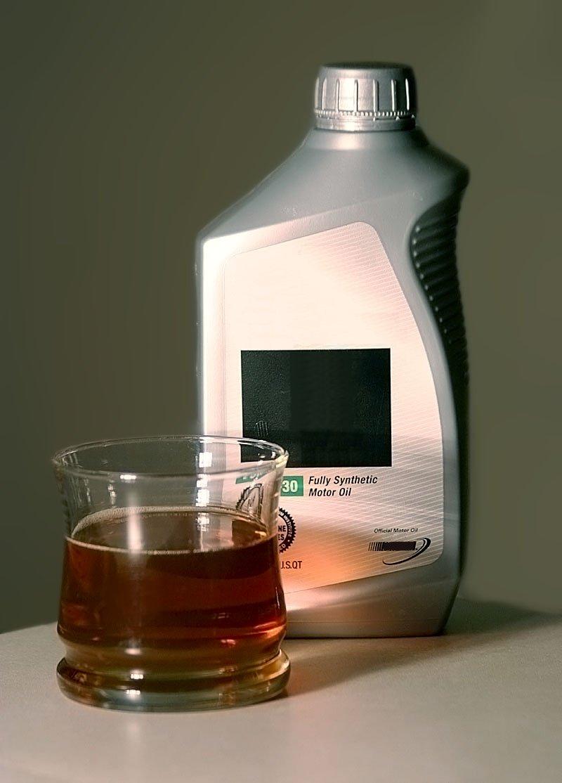 Flaske med motoroje og et glass fylt med olje foran. foto.