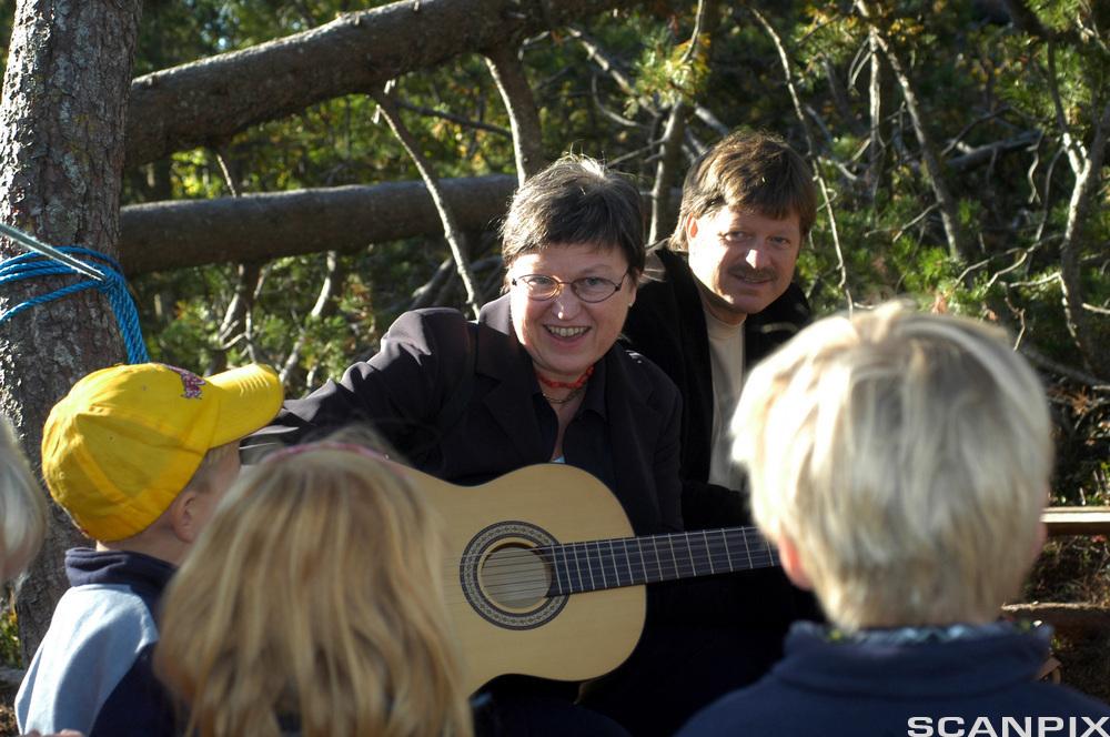  En kvinne spiller gitar for tre barn. Foto.