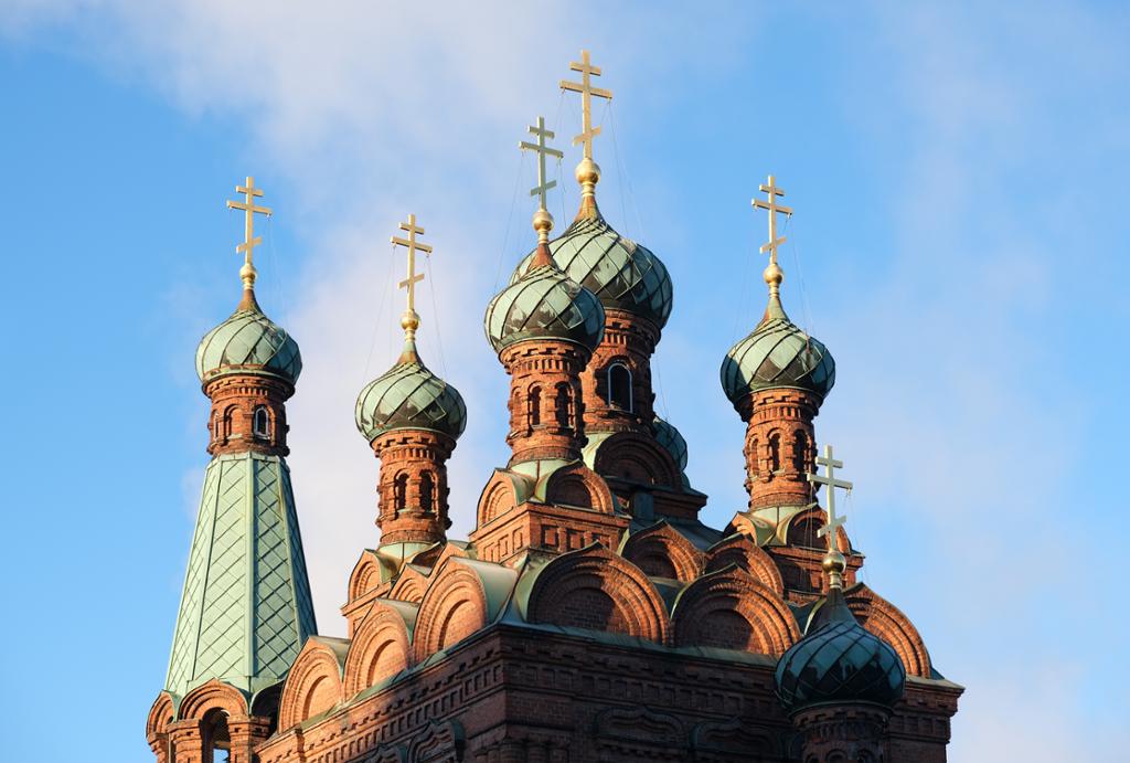 Kirkespir med løkformede kupler og kors med tre tverrbjelker. Kirka er i fargene brunt og lysegrønt. Foto.