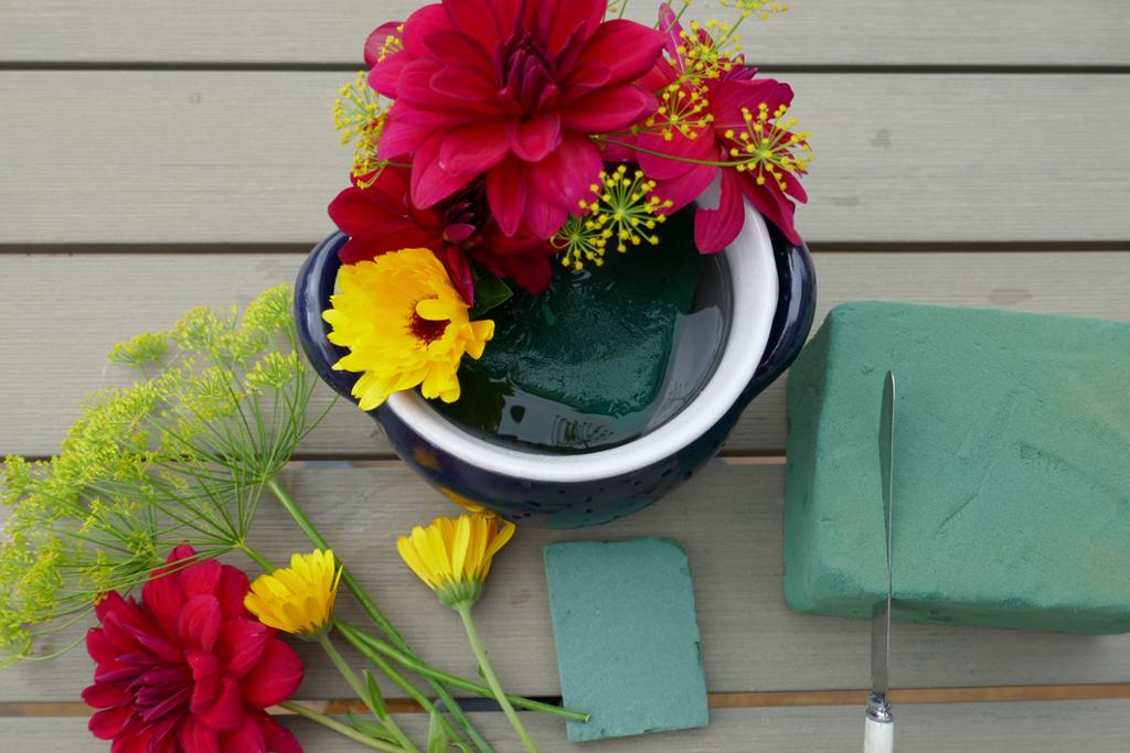 Gule og raude blomstrar ligg på bord ved sida av blomsteroppsats. Gule og raude blomstrar stukke ned i oasis. Foto.
