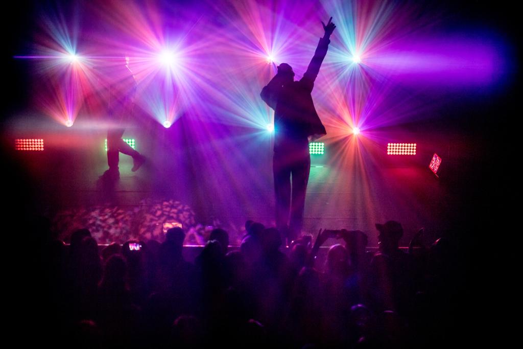 Silhuett av en sanger på en scene med publikum foran. Scenelysene er røde, lilla og blå. Foto. 