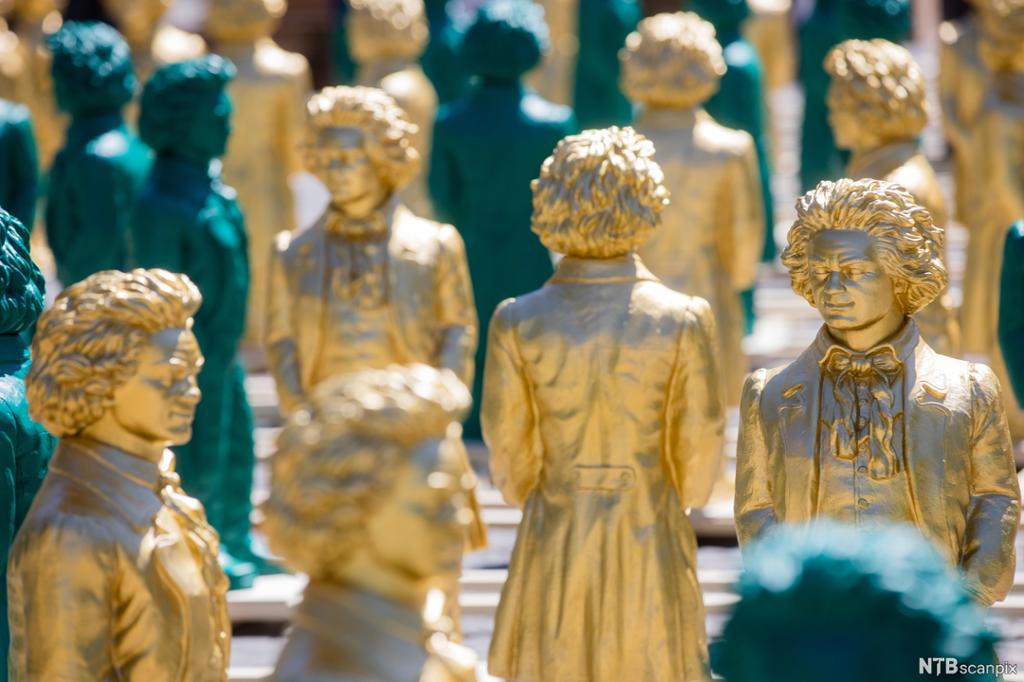 Et mylder av små, smilende Beethoven-statuer, mange i gull, noen i grønt. Foto.