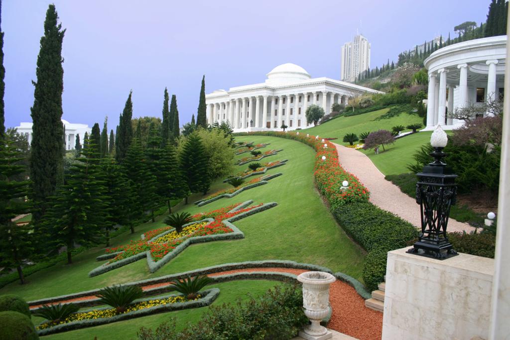 Monumentalt hvitt bygg med søyler omgitt av en rikt utsmykket hage. Foto.
