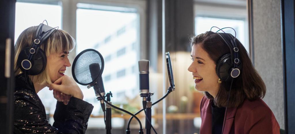 To kvinner sit i eit radiostudio. Begge smiler. Foto.