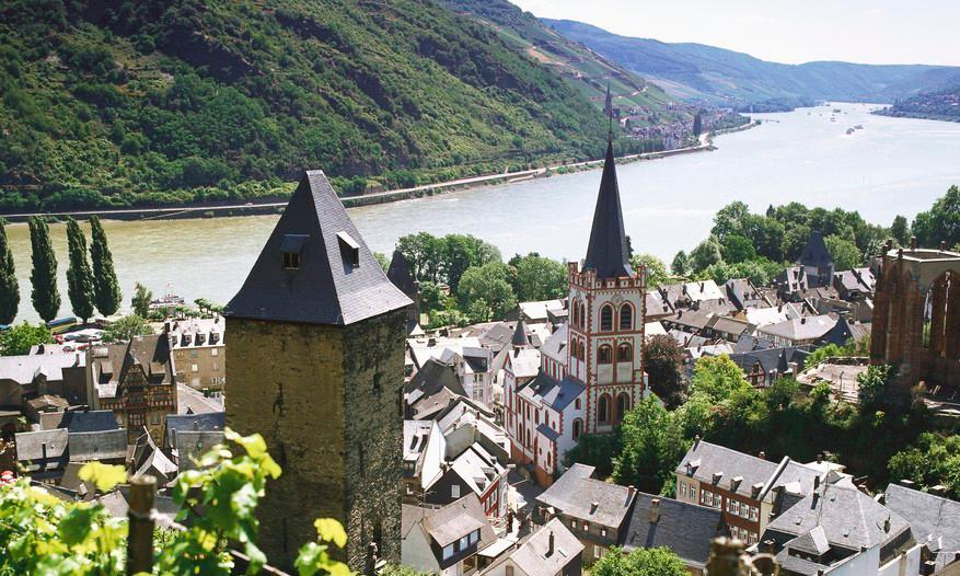 Foto av landsbyen Bacharach med elva Rhinen og skrånende åssider i bakgrunnen.