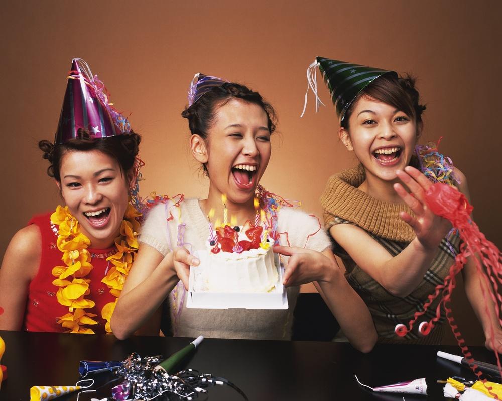 Tre jenter med papirhattar, girlandrar og bursdagskake med lys. Foto.