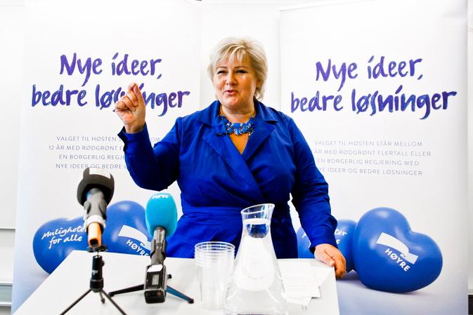 Erna Solberg står foran valgplakater med slagord. Foto