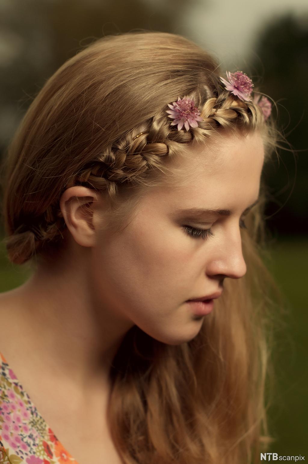 Flette og blomster i håret på ung kvinne. Foto.
