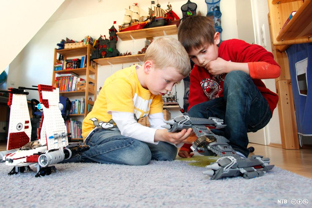 To gutter leker med lego, byggeklosser og Star Warsfigurer, på gulvet på et barnerom. Foto.
