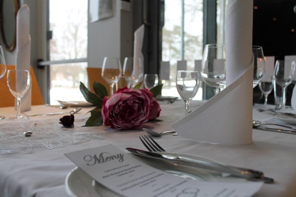 Pent dekt bord med kvit duk, kvite serviettar og ein rosa peon som pynt. Foto.