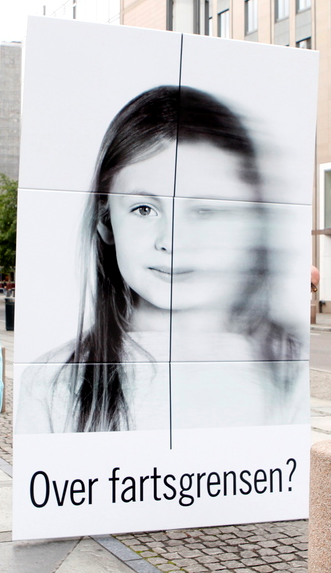 Et stort skilt viser et portrettbilde av ei lita jente med langt, mørkt hår. En loddrett strek deler bildet i to. Til venstre er bildet skarpt, men til høyre er bildet uklart og diffust som om det er tatt i fart. Under bildet står teksten «Over fartsgrensen?». Foto.