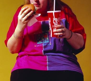 Overvektig jente som spiser burger og drikker cola til. Foto.