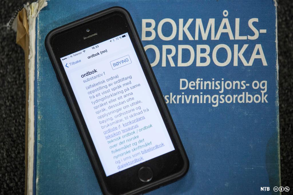 Mobiltelefon ligger på ei bokmålsordbok. Mobilskjermen viser ordboka som mobil-app. Foto.