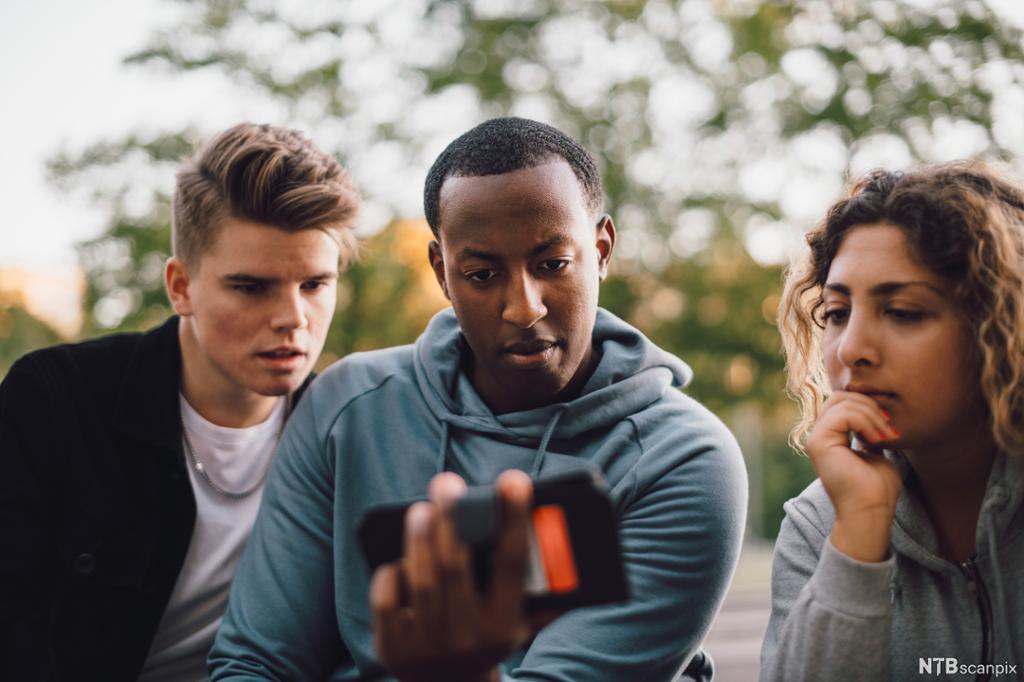 Tre ungdommar ser på ein mobilskjerm. Foto.