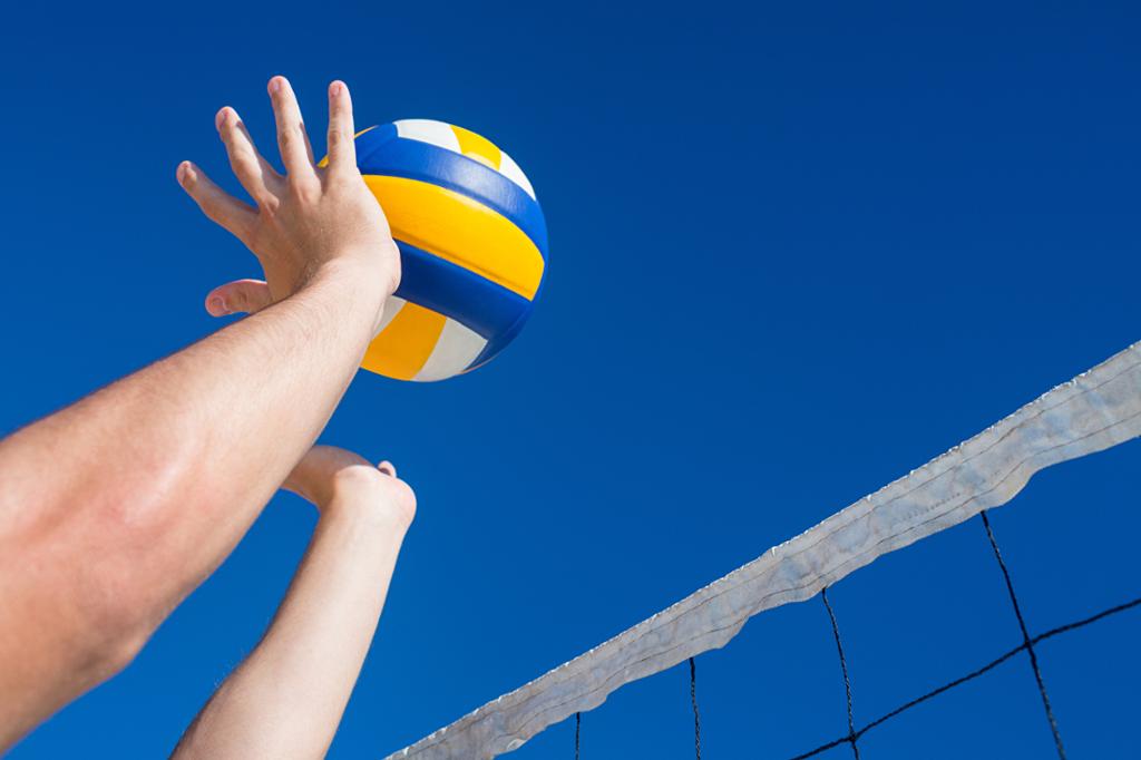 Hender som slår en volleyball over et nett. Foto.