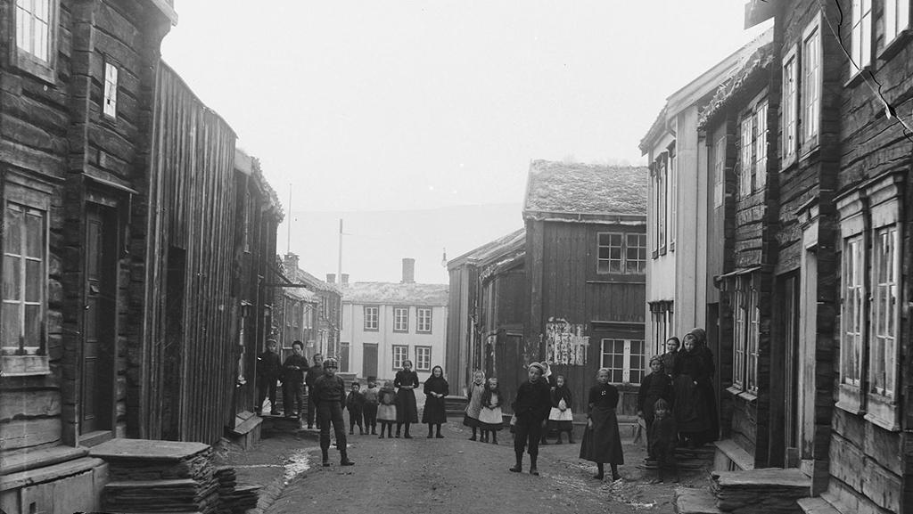 Bygate med trehus i Røros på slutten av 1800-talet. Barn og kvinner står i gata og ser i kamera. Foto.