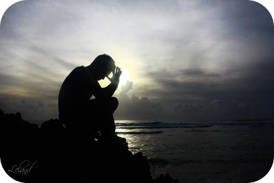 Mann sitter ved havet og ber i solnedgangen. Foto.