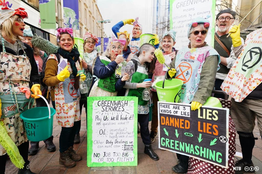 Mennesker kledd ut som vaskere. De har vaskeutstyr og plakater og protesterer mot grønnvasking. Foto. 